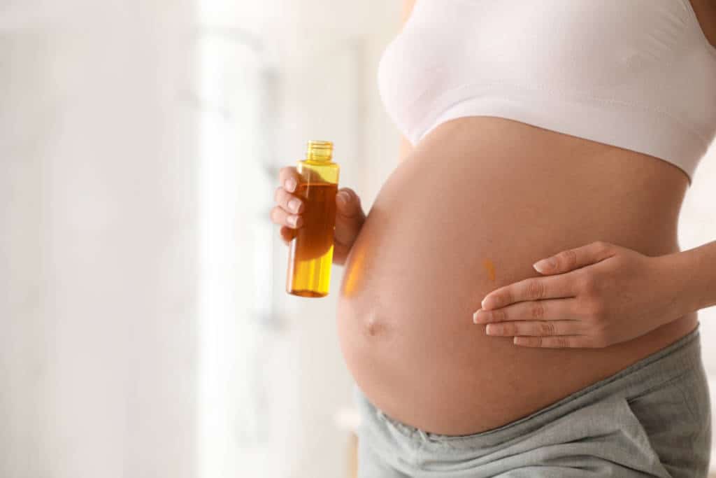 jeune femme enceinte se met de l'huile sur le ventre