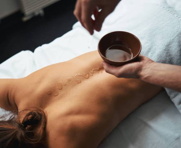Pretty unrecognized female client lying on massage bed while massage therapist putting aroma oil on her back in spa salon